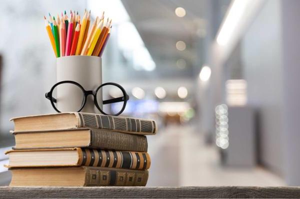 books, glasses and colored pencils stacked on a desk